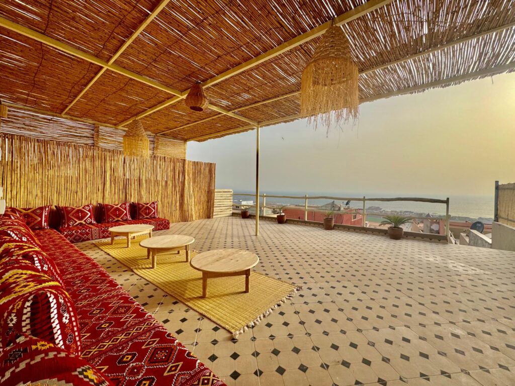 Exterior view of Tamraght surf house Morocco at golden hour — whitewashed walls, rooftop terrace, Atlantic Ocean in background